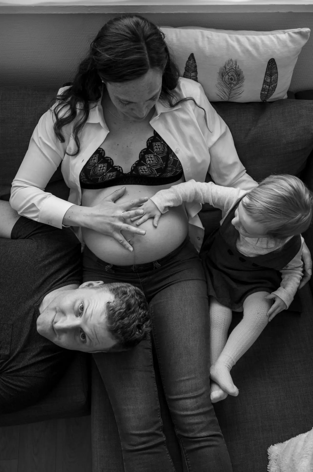 photographie d'un câlin en famille sur le canapé avec une femme grossesse le père et la grande soeur