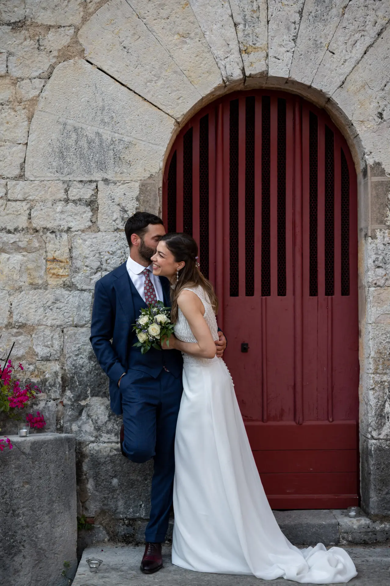 Jeunes mariés complices devant porte rouge de La Chapelle