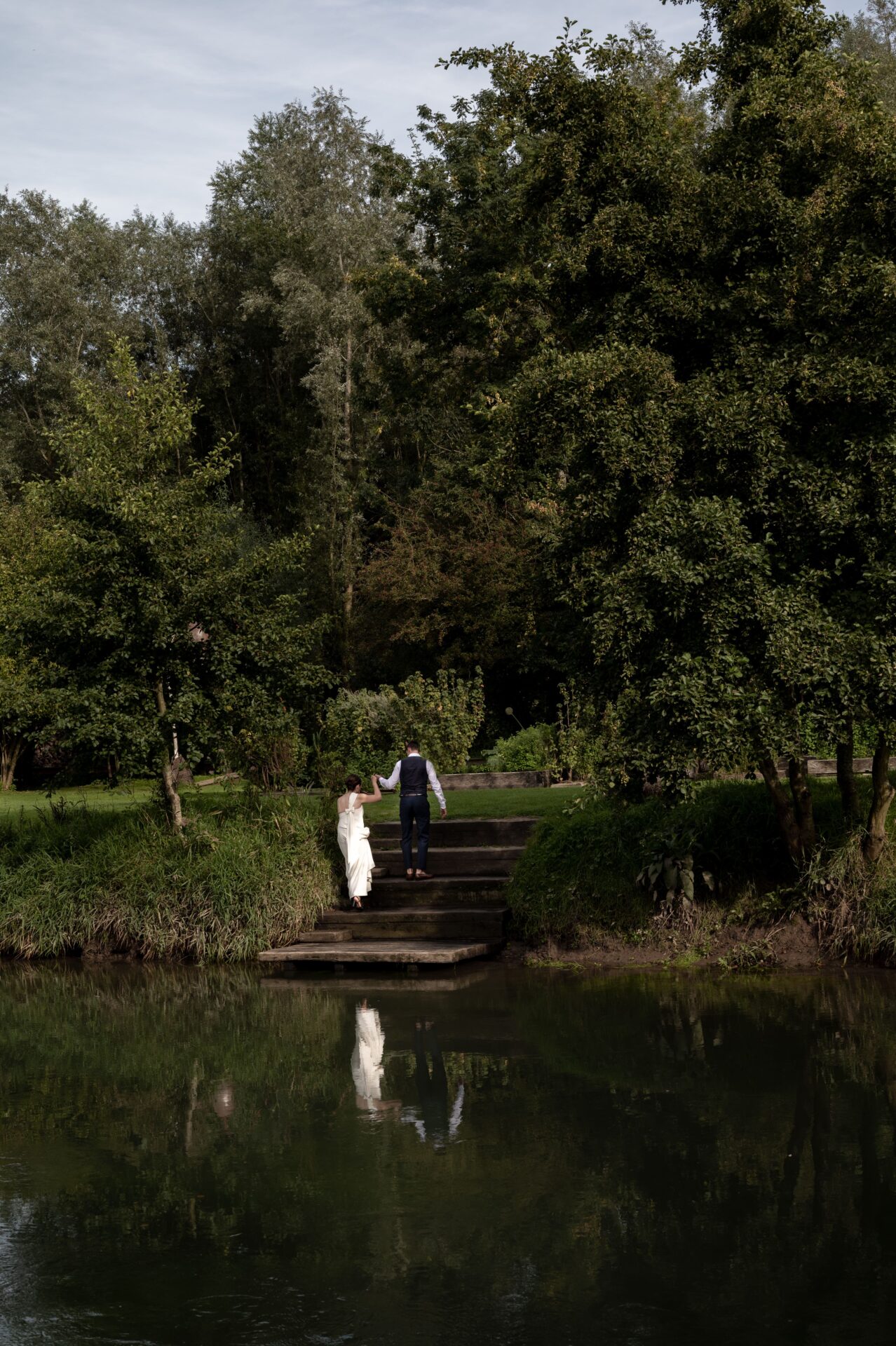 couple de jeunes mariés marchent au-dessus d'un lac dans lequel ils se reflètent