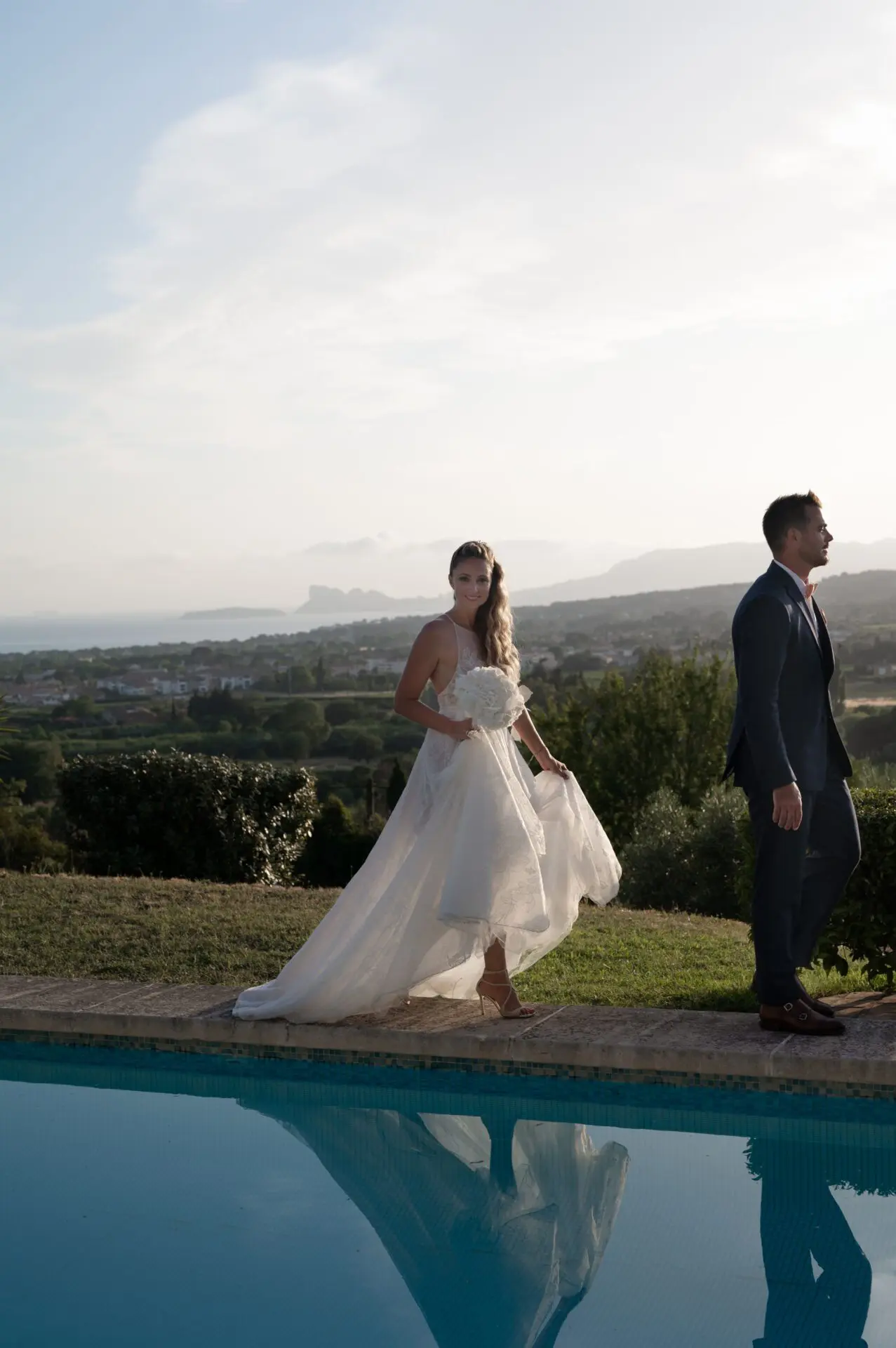 couple de jeunes mariés marchent près d'une piscine avec une vue sur la provence