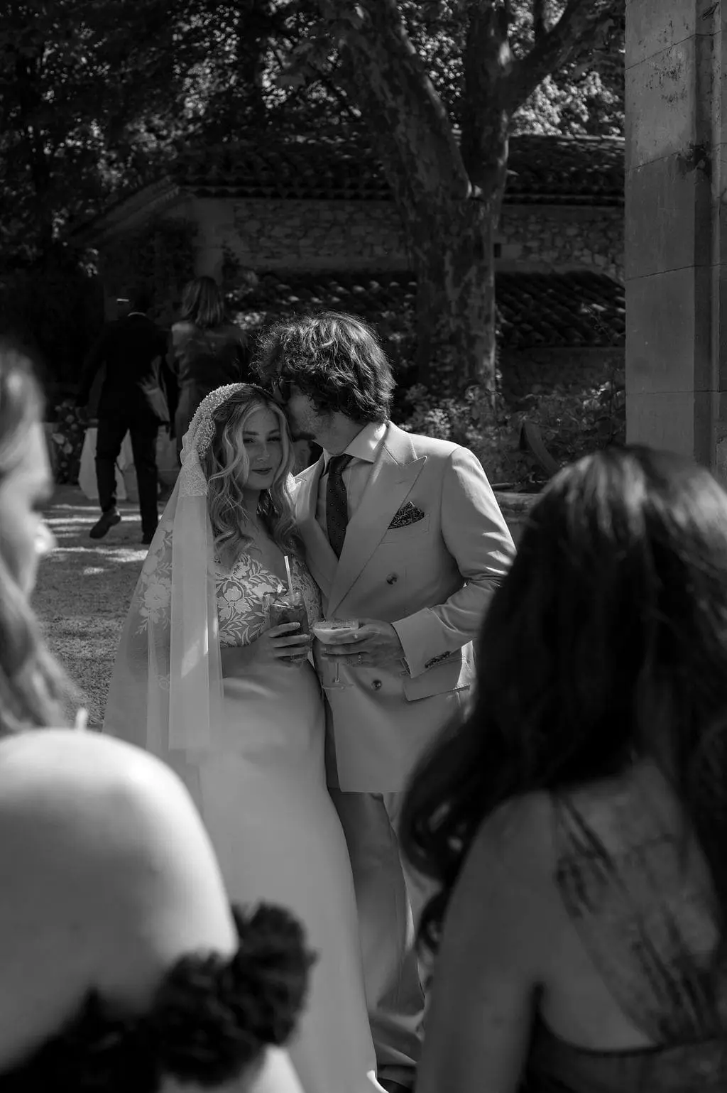 groom kissing his wife on the forehead while drinking a cocktail