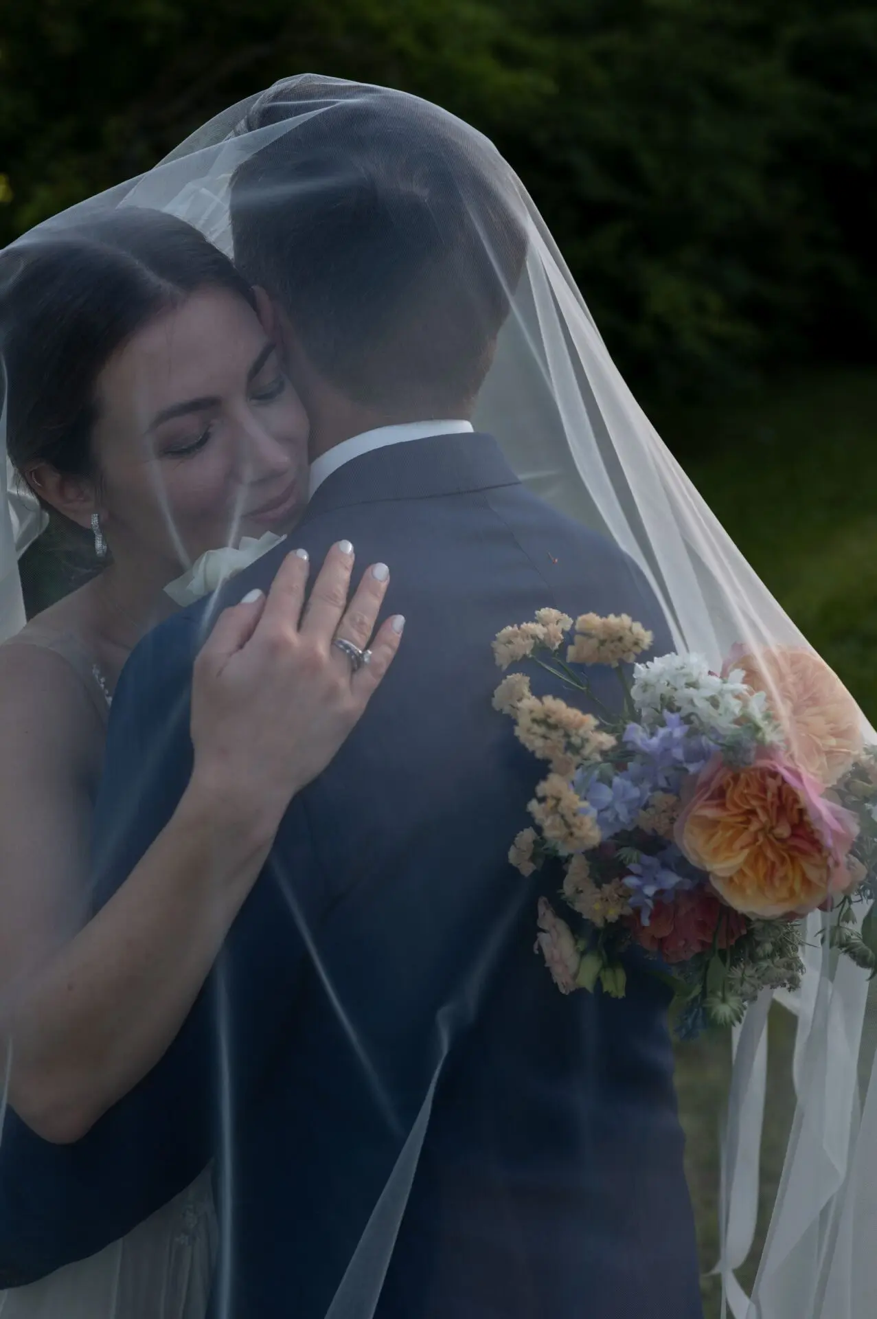 bride holding her bouquet under her veil hugging her newly husband