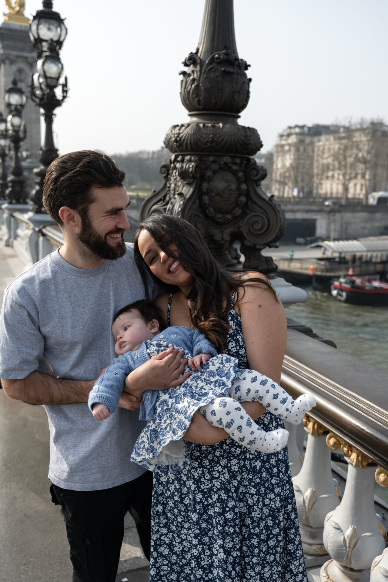 couple s'enlacent et rient avec leur nouveau-née dans les bras sur le pont Alexandre III